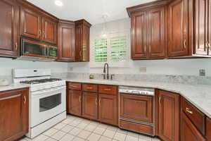 Custom Cherry cabinets from Barlows featuring gas range gas stove, decorative light fixtures, dishwasher, large single tub sink, and light tile floors