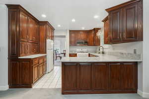 Kitchen featuring kitchen peninsula, white appliances, beautiful quartz counters, hanging light fixtures, and sink