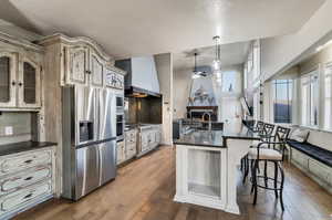 Kitchen featuring wall chimney range hood, a center island with sink, stainless steel appliances, hardwood / wood-style flooring, and sink