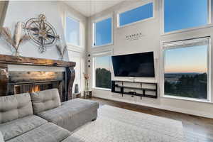 Living room with a high ceiling, a tiled fireplace, a healthy amount of sunlight, and dark wood-type flooring