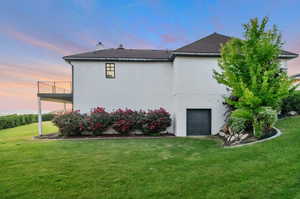 Property exterior at dusk with a garage, a yard, and a balcony