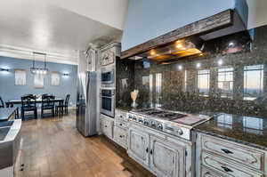 Kitchen with light wood-type flooring, decorative light fixtures, backsplash, wall chimney range hood, and appliances with stainless steel finishes