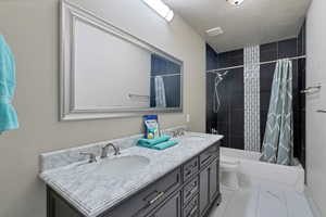 Full bathroom featuring shower / tub combo, double sink, tile floors, vanity with extensive cabinet space, and toilet