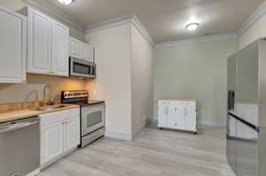 Kitchen with stainless steel appliances, light hardwood / wood-style floors, white cabinets, and sink