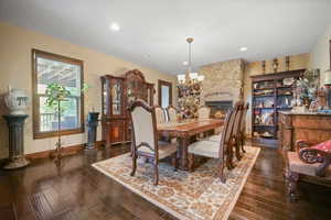 Dining room featuring a stone fireplace, a chandelier, and dark hardwood / wood-style floors