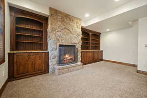 Unfurnished living room featuring a stone fireplace, carpet flooring, and built in shelves