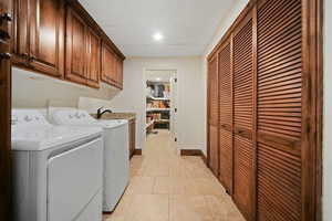 Clothes washing area featuring cabinets, separate washer and dryer, and light tile floors