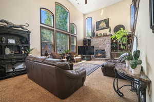 Living room featuring a stone fireplace, high vaulted ceiling, carpet floors, and ceiling fan