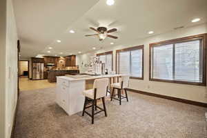 Kitchen featuring white cabinetry, appliances with stainless steel finishes, a breakfast bar, ceiling fan, and light colored carpet