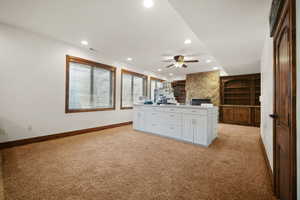 Kitchen featuring a fireplace, white cabinets, built in features, ceiling fan, and light colored carpet