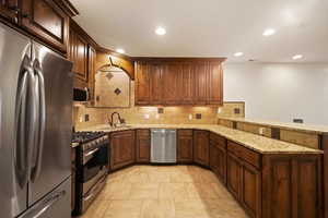 Kitchen featuring light stone counters, light tile flooring, kitchen peninsula, tasteful backsplash, and appliances with stainless steel finishes