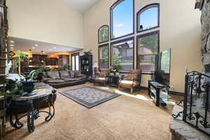 Carpeted living room with a stone fireplace and a towering ceiling