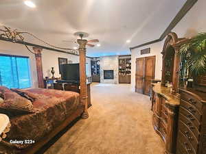 Carpeted bedroom with ceiling fan, crown molding, and a stone fireplace