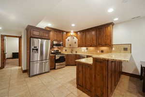 Kitchen with light stone countertops, kitchen peninsula, tasteful backsplash, stainless steel appliances, and light tile floors