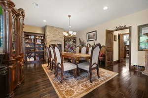 Dining area featuring a stone fireplace, decorative columns, a chandelier, and dark wood-type flooring