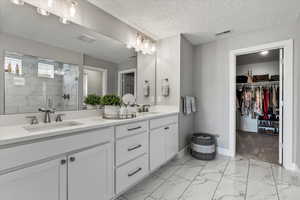 Bathroom featuring walk in shower, a textured ceiling, dual vanity, and tile floors