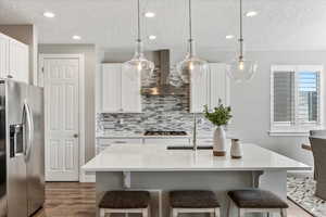 Kitchen with decorative light fixtures, backsplash, hardwood / wood-style floors, wall chimney exhaust hood, and appliances with stainless steel finishes