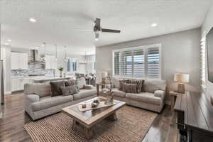 Living room with ceiling fan with notable chandelier, a textured ceiling, sink, and dark wood-type flooring