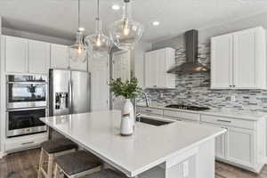 Kitchen with stainless steel appliances, wall chimney range hood, backsplash, and a kitchen island with sink