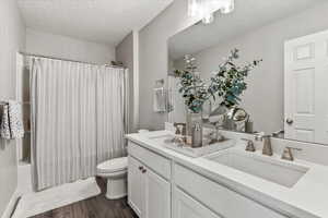 Full bathroom with wood-type flooring, vanity with extensive cabinet space, toilet, and a textured ceiling