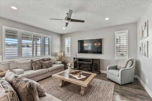 Living room with a textured ceiling, dark wood-type flooring, and ceiling fan