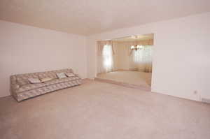 Unfurnished living room with carpet floors, a textured ceiling, and a chandelier