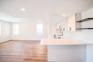 Kitchen with white cabinetry, kitchen peninsula, light wood-type flooring, a textured ceiling, and sink