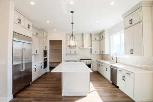 Kitchen featuring hanging light fixtures, a kitchen island, wall chimney exhaust hood, built in appliances, and dark hardwood / wood-style floors