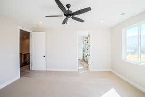 Unfurnished bedroom featuring ceiling fan, light colored carpet, and ensuite bath