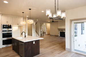 Kitchen featuring decorative light fixtures, an island with sink, sink, a stone fireplace, and light hardwood / wood-style floors