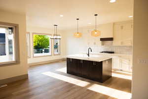 Kitchen featuring decorative backsplash, a kitchen island with sink, white cabinetry, and light hardwood / wood-style floors