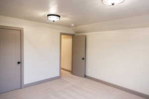 Spare room with light carpet, vaulted ceiling, and a textured ceiling