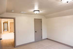 Unfurnished room with vaulted ceiling, a textured ceiling, and light colored carpet