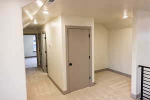 Hallway with light colored carpet and vaulted ceiling