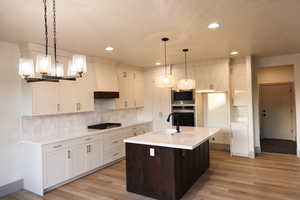 Kitchen featuring sink, light wood-type flooring, decorative light fixtures, and custom exhaust hood