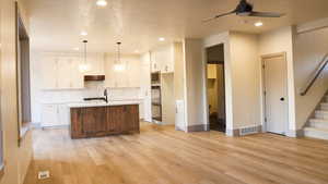 Kitchen with an island with sink, hanging light fixtures, light hardwood / wood-style flooring, backsplash, and white cabinets