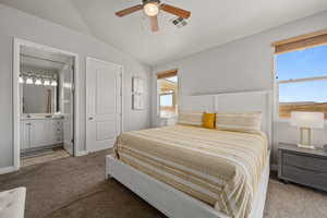 Carpeted bedroom featuring connected bathroom, lofted ceiling, multiple windows, and ceiling fan