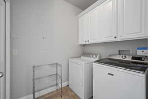 Clothes washing area featuring hookup for a washing machine, cabinets, light tile floors, and washing machine and dryer