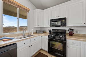 Kitchen featuring black appliances, sink, white cabinets, and light tile flooring