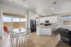 Kitchen with white cabinets, black appliances, light tile floors, and lofted ceiling