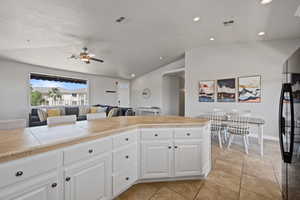 Kitchen with white cabinetry, lofted ceiling, black refrigerator, ceiling fan, and light tile floors