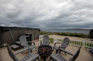 View of terrace with an outdoor fire pit, oversized hot tub, and a water view