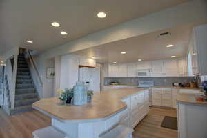 Kitchen with light hardwood / wood-style flooring, backsplash, white cabinets, sink, and white appliances