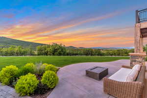 Patio terrace at dusk featuring a mountain view, a fire pit, and a lawn