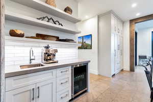 Kitchen featuring wine cooler, backsplash, light tile floors, sink, and white cabinets