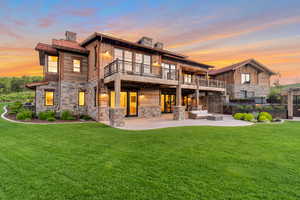 Back house at dusk with a yard, an outdoor living space, a balcony, and a patio