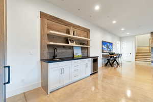 Kitchen with wine cooler, sink, backsplash, and white cabinetry