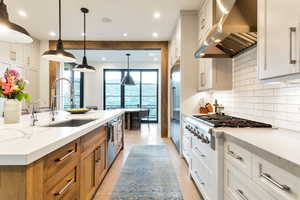 Kitchen featuring tasteful backsplash, a kitchen island with sink, light stone countertops, wall chimney exhaust hood, and light tile floors