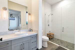 Bathroom with a shower with door, tile flooring, toilet, and vanity