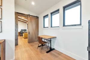 Home office featuring a barn door, light hardwood / wood-style floors, and lofted ceiling